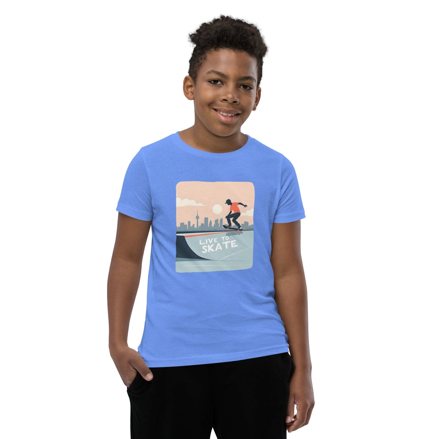 Boy wearing a blue youth T-shirt with a skateboarding graphic and city skyline, reading “Live to Skate”
