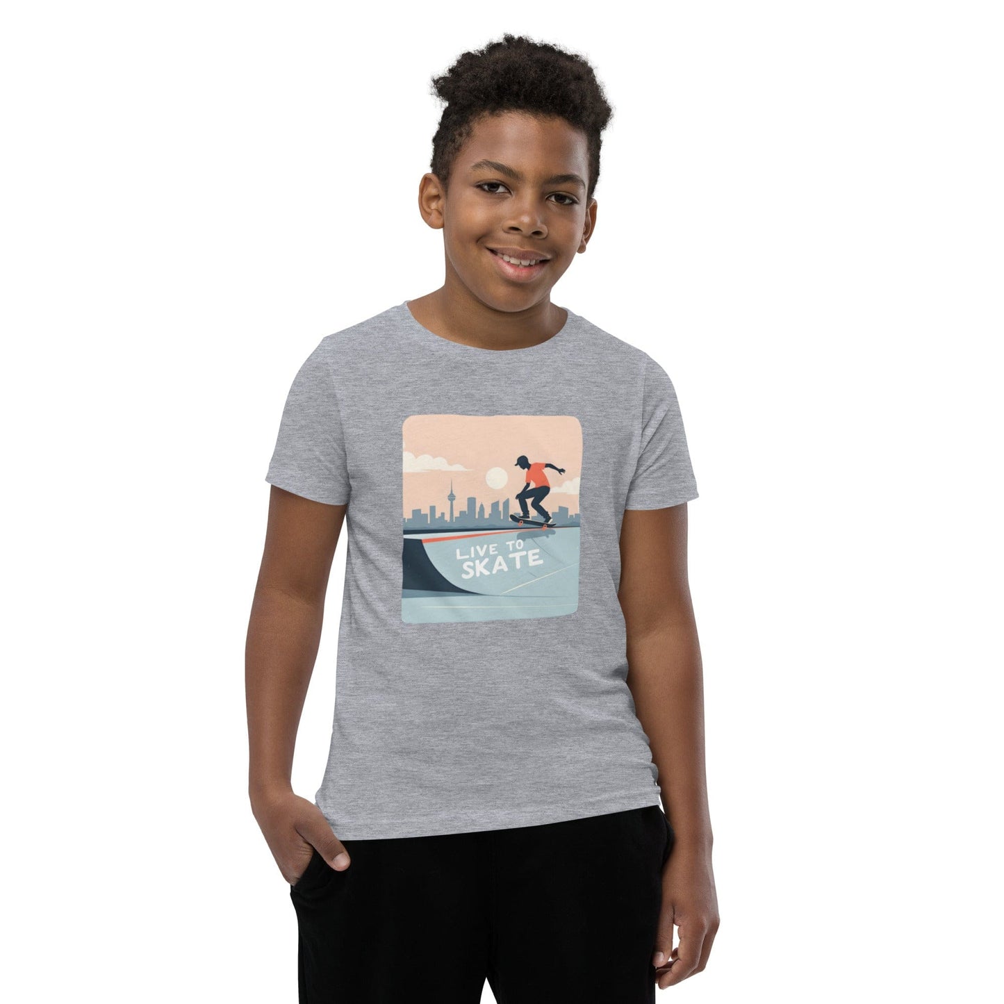 Boy wearing a grey youth T-shirt with a skateboarding graphic and city skyline, reading “Live to Skate”