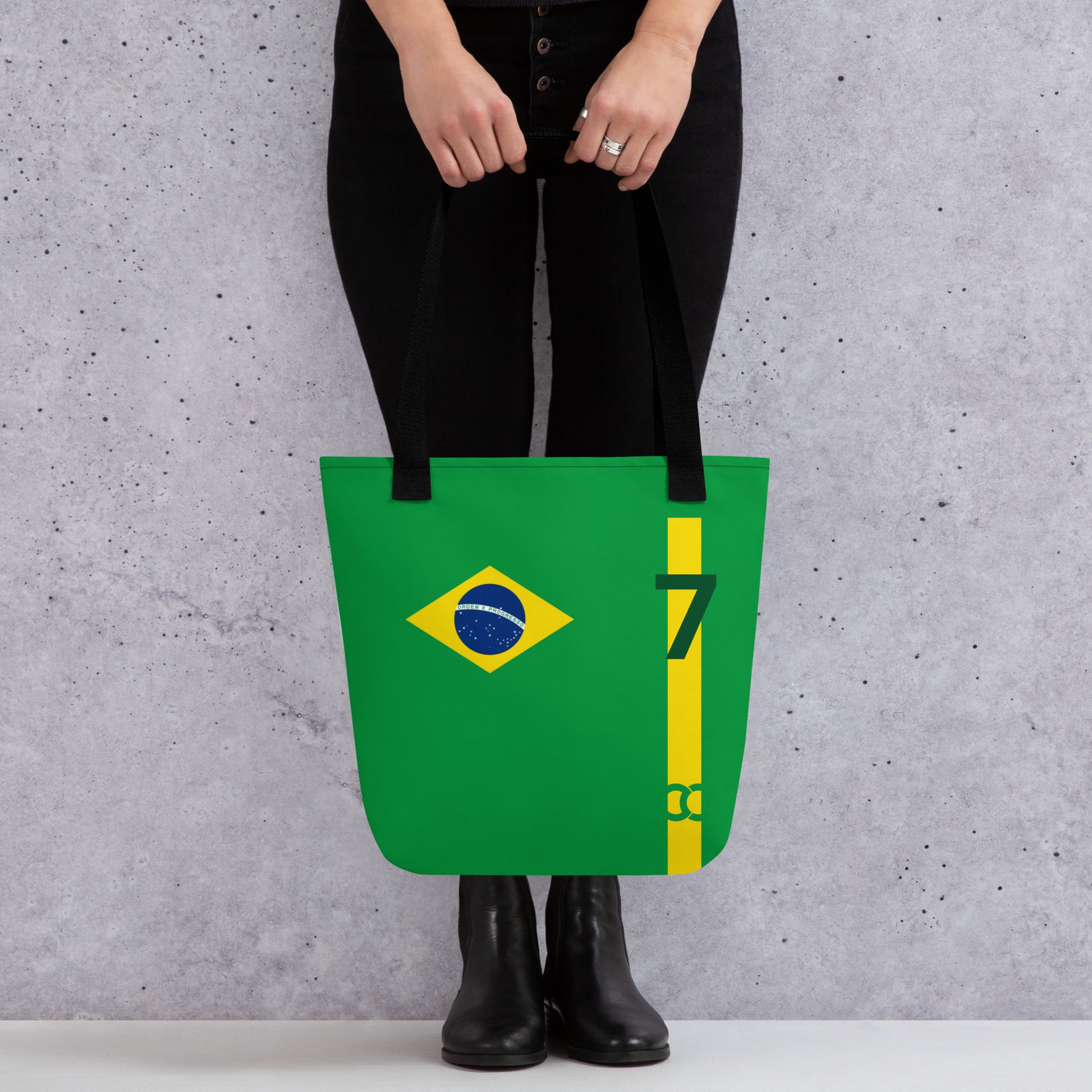 Green tote bag held by a model, featuring a yellow vertical stripe, the Brazil flag, number 7, and ccanvas logo near the bottom edge